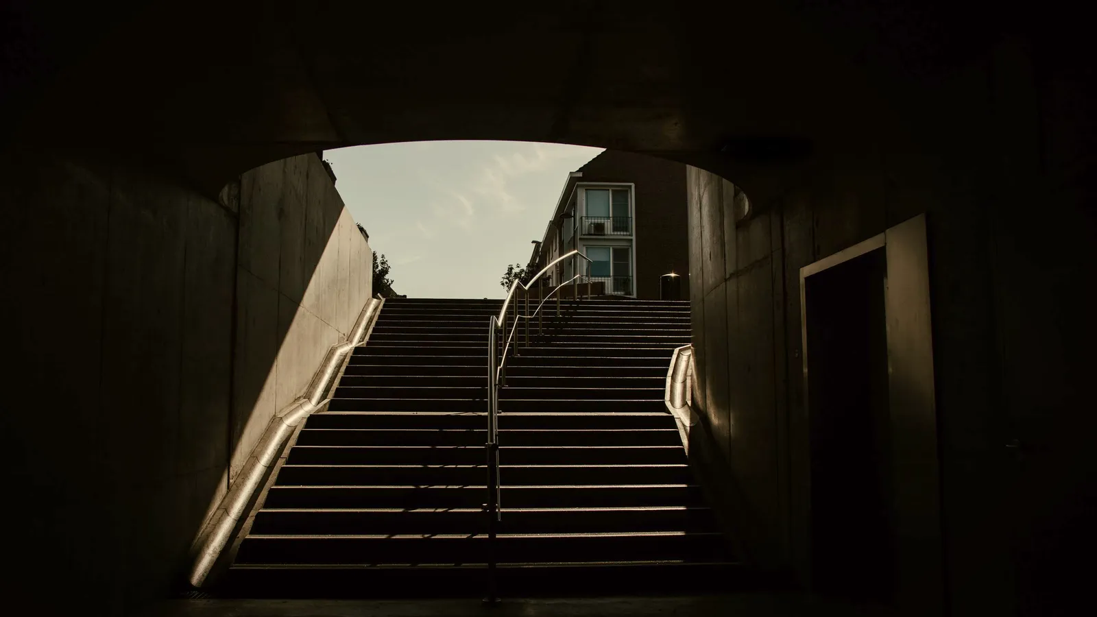 An empty flight of concrete steps rising out of a dark passage toward an open sky.